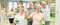 Dans une salle de sport, deux femmes âgées aux cheveux blonds et deux hommes âgés aux cheveux blancs tiennent des tapis d'exercice verts et envoient la main en souriant