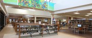 Dans une bibliothèque, plusieurs étagères de livres sont enlignées l'une après l'autre. Une table avec des ordinateurs se trouve à droite et une fresque colorée se trouve près du plafond.