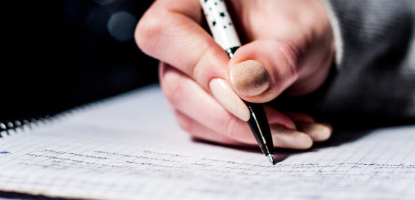 Main blanche avec vernis beige écrit dans un cahier de notes avec un crayon noir et blanc