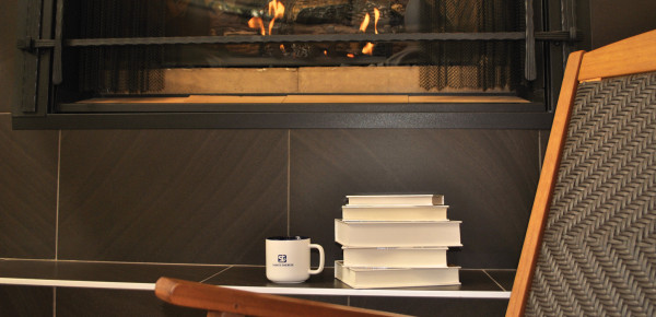 Pile de livres et tasse à café blanche avec le logo de Sainte-Thérèse placés sur une table en face d'un foyer allumé