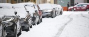 Plusieurs voitures recouvertes de neige sont alignées l'une en arrière de l'autre en bordure de rue