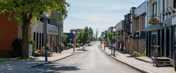 Rue Turgeon avec un arbre feuillu, la Maison du citoyen et le cabaret BMO à gauche, et des commerces variés à droite