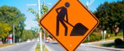 Installé sur un terre-plein au milieu d'une rue se trouve une pancarte orange avec un symbole d'un travailleur de la construction en noir