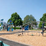 À l'extérieur, module de jeux bleu et vert avec glissades, balançoires pour jeunes enfants et stations d'escalade