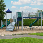 À l'extérieur, modules de jeux gris, verts et bleus avec glissades, stations d'escalade et d'équilibre