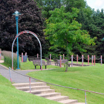 À l'extérieur près d'une forêt, sentier en béton avec des arches installées aux intersections et des bancs de parcs placés sur les côtés