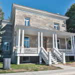 Maison de briques grises avec une grand patio avant et une balustrade blanche.
