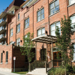 Grand bâtiment droit fait de briques rouges avec un escalier en béton menant à la porte d'entrée fenêtrée rouge