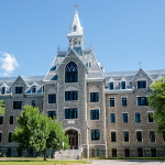 Grand bâtiment de pierres grises avec des tourelles en pointes sur lesquelles figurent des crucifix