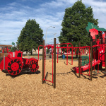 À l'extérieur, module de jeux rouge avec glissades, stations d'escalade et tracteur