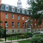 Bâtiment rectangulaire de briques rouges avec plusieurs fenêtres blanches alignées sur quatre étages.