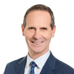 Homme blanc avec cheveux bruns et blancs porte un tailleur bleu marin