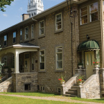 Bâtiments de pierre grise avec deux portes blanches dont une est recouverte d'un auvent vert forêt