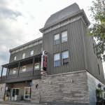 Bâtiment de trois étages tout en gris avec une enseigne verticale sur laquelle est écrit Bar en rouge sur fond noir
