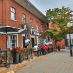 Bâtiment de briques rouges avec l'enseigne du café Les Allumées et des personnes prennent un café et mangent sur la terrasse extérieure