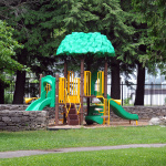 À l'extérieur, module de jeux en forme d'arbre avec des glissades vertes et des barreaux jaunes